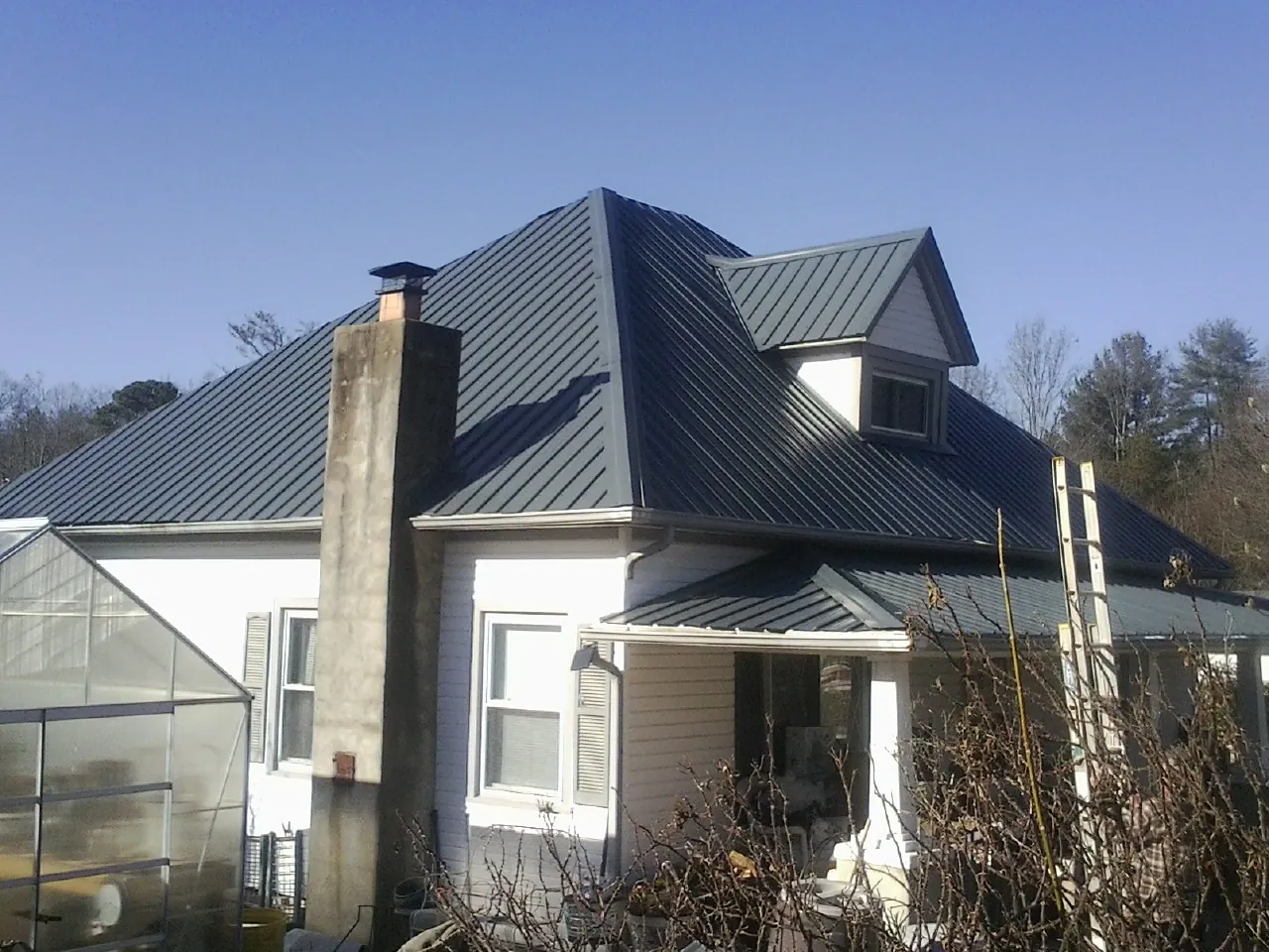 Dark blue standing seam metal roof on a white farmhouse with dormer — Slate & Tile Roof Repair by Roofing Brothers in Bacliff