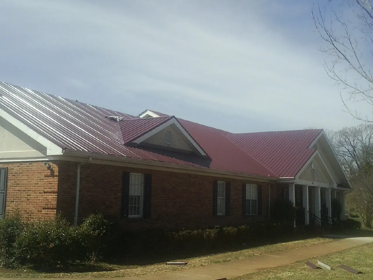 Red metal roof with gabled entries on a long brick building, from a Hail Damage Roof Repair job in Bacliff