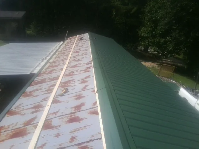 Old rusted panels beside newly installed green metal roofing — Wind Damage Roof Repair by Roofing Brothers in Bacliff