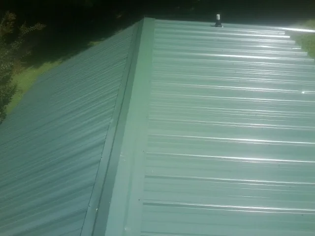 New green metal panels meeting at the ridge of a roof — Flat Roof Repair work by our crew in Bacliff