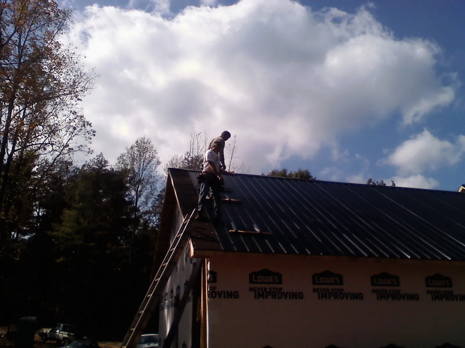 Roofer fastening dark metal panels high against a cloudy sky, from a Roof Inspection job in Bacliff