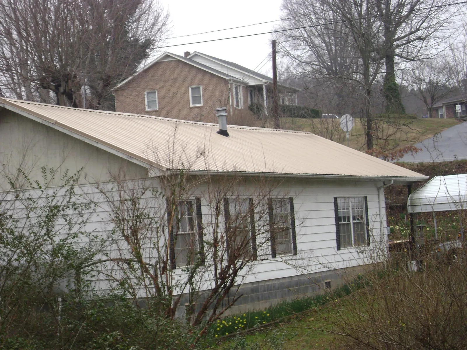 Tan metal roof on a white sided house set into a hillside — Commercial Roofing by Roofing Brothers in Bacliff